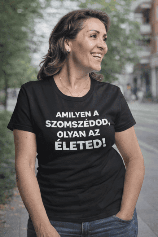 Előtérben boldog nő fekete pólóban, városi környezetben, kedves mosoly, barátságos hangulat.