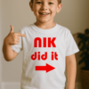 Gyerek fiú póló, "NIK did it" felirattal, piros nyíllal, otthoni környezetben.