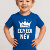 Egy fiatal fiú mosolyog, kék pólón, amelyen "Herceg" és "Egyedi Név" felirat található, fehér koroná.