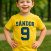 Sárga gyermek póló, SÁNDOR 9 felirattal, parkban játszó kisfiú.