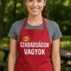 Szabadságon vagyok feliratos vörös kötény, mosolygó fiatal nő szabadban, parkban.