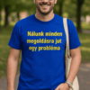 Az ember mosolyogva áll parkban, kék pólóban, felirattal: "Nálunk minden megoldásra jut egy probléma.