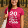 Fiatal nő mosolyog az őszi parkban, pink pólóban, 20 éves és egyedi szép felirattal.