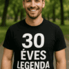 Férfi mosolygós, fekete póló, "30 ÉVES LEGENDA" felirattal, parkban, természetes fényben.