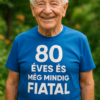 80 éves és még mindig fiatal feliratú kék pólós idős férfi mosolyog a természetben.