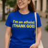 Szabadtéri kép egy mosolygó nővel, aki kék pólót visel, "I'm an atheist (THANK GOD)" felirattal.
