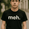 Férfi fiatalember utcai környezetben, fekete "meh." feliratú pólóval.