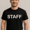 Személy, aki STAFF feliratú pólót visel, mosolyogva áll a fehér háttér előtt.